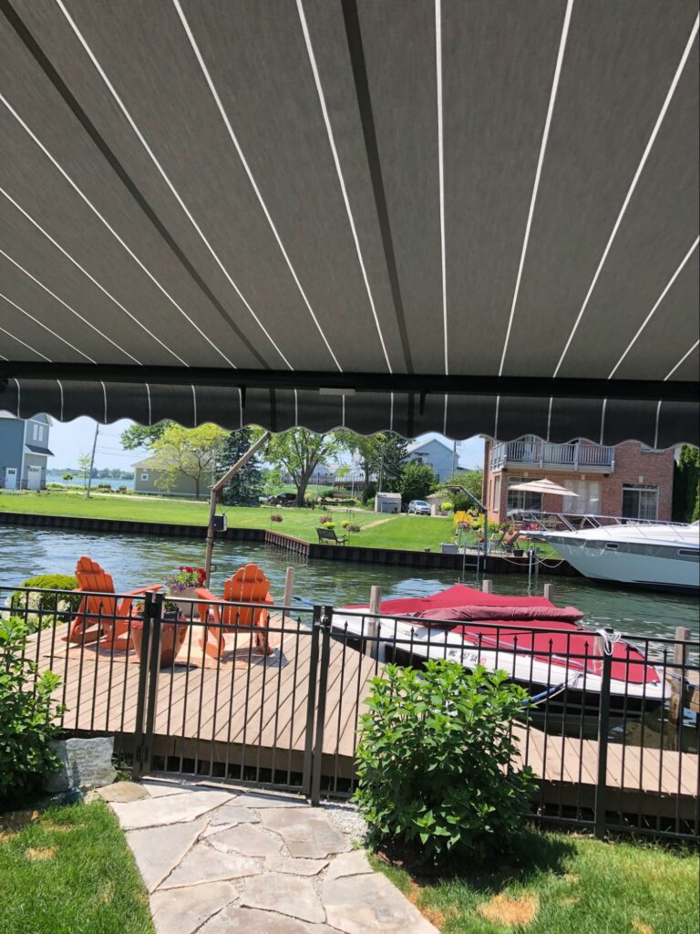 Home along the water featuring rolling striped awning for their lanai Miami, Florida retractable deck roof | Sun Protection