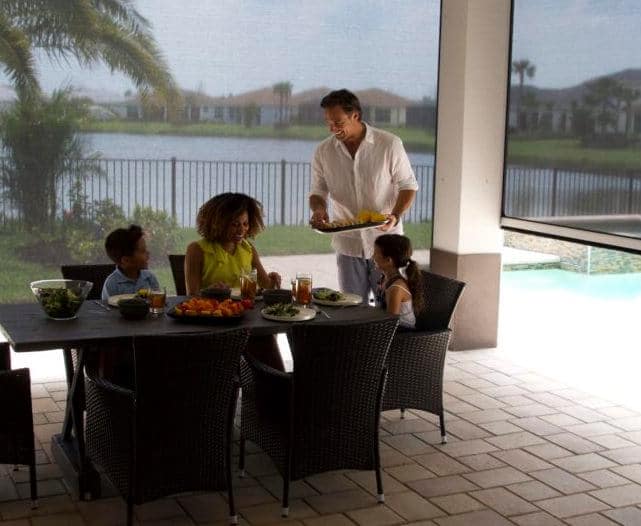 A family enjoys a meal on their patio with their motorized retractable screens down for blocking the sun and insects. | Sun Protection