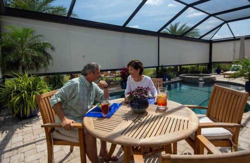 A couple enjoys a private lunch by the pool. They have opted for multiple motorized privacy screens for maximum coverage at the push of a button. See options here.