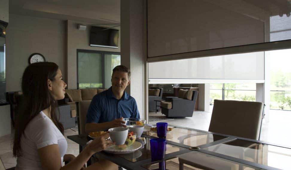 A couple enjoys brunch on their Florida patio. They chose to release the motorized screen to the height that worked for them. These mesh screens can go all the way to the floor.