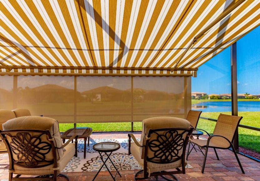 A relaxing patio with water-front views features a beautiful tan striped awning and a drop-down screen for blocking the afternoon sun.| Sun Protection