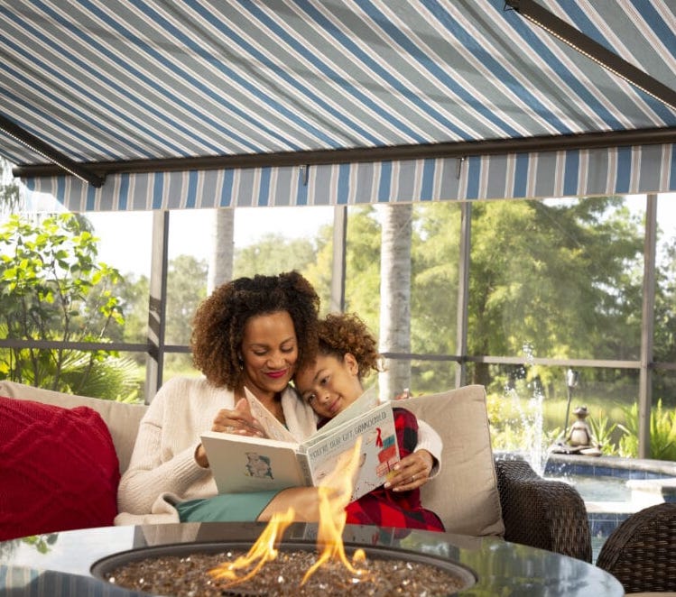 A mom and her son relax and read a book under the shade of their retractable motorized patio awning. Learn how you can benefit from an awning all year long.