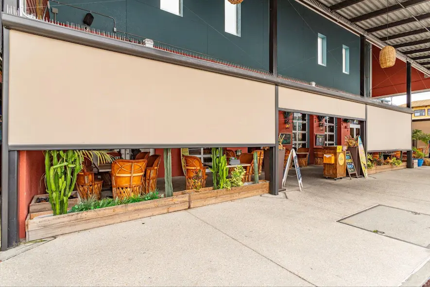 Retractable motorized sun screens are pulled partially down to provide shade to an outdoor dining area.