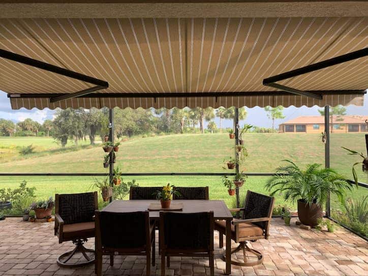 A patio overlooking a large green yard, with a retractable awning over an outdoor dining set.