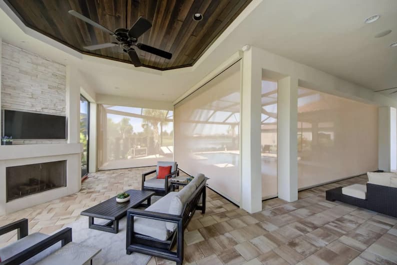 An enclosed sitting area with fireplace and ceiling fan protected with retractable motorized solar shades.